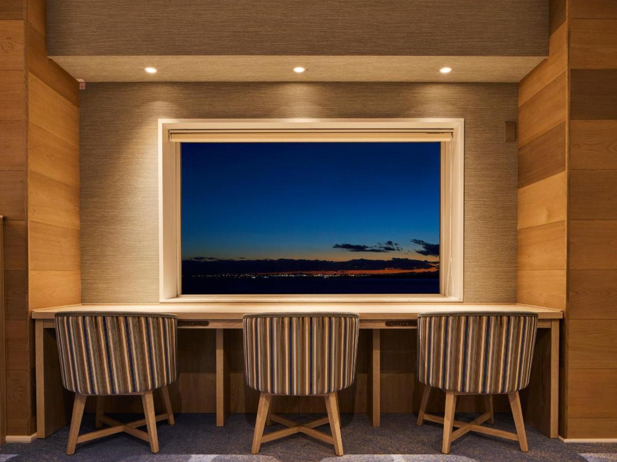 Grand Nikko Tokyo Bay Maihama Otel Urayasu Dış mekan fotoğraf The photo depicts a cozy workspace or study area featuring a long, minimalist desk with three chairs. The wall behind the desk is made of wood, creating a warm atmosphere. At the center, there is a large window that showcases a beautiful evening view