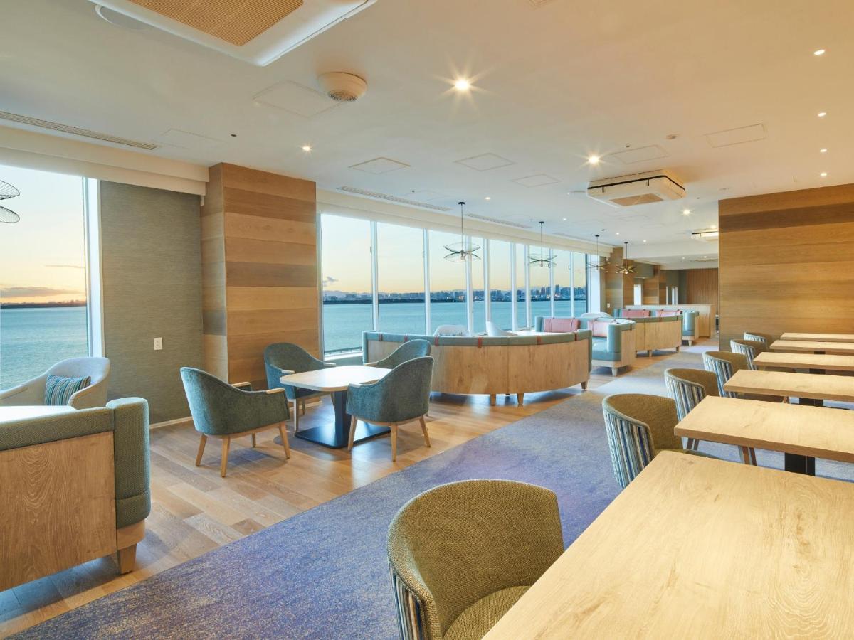 Grand Nikko Tokyo Bay Maihama Otel Urayasu Dış mekan fotoğraf The photo shows a modern interior space, likely a dining or lounge area. It features large windows that offer a view of the water, allowing natural light to fill the room. The decor includes wooden walls and stylish, comfortable furniture, with sever