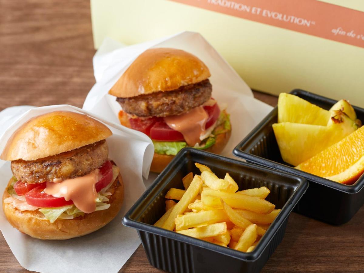 Grand Nikko Tokyo Bay Maihama Otel Urayasu Dış mekan fotoğraf The photo shows two small burgers placed on a white background, each with a golden-brown bun, a fried patty, lettuce, tomato, and a creamy sauce. Alongside the burgers, there are two containers: one holding a serving of french fries and the other con