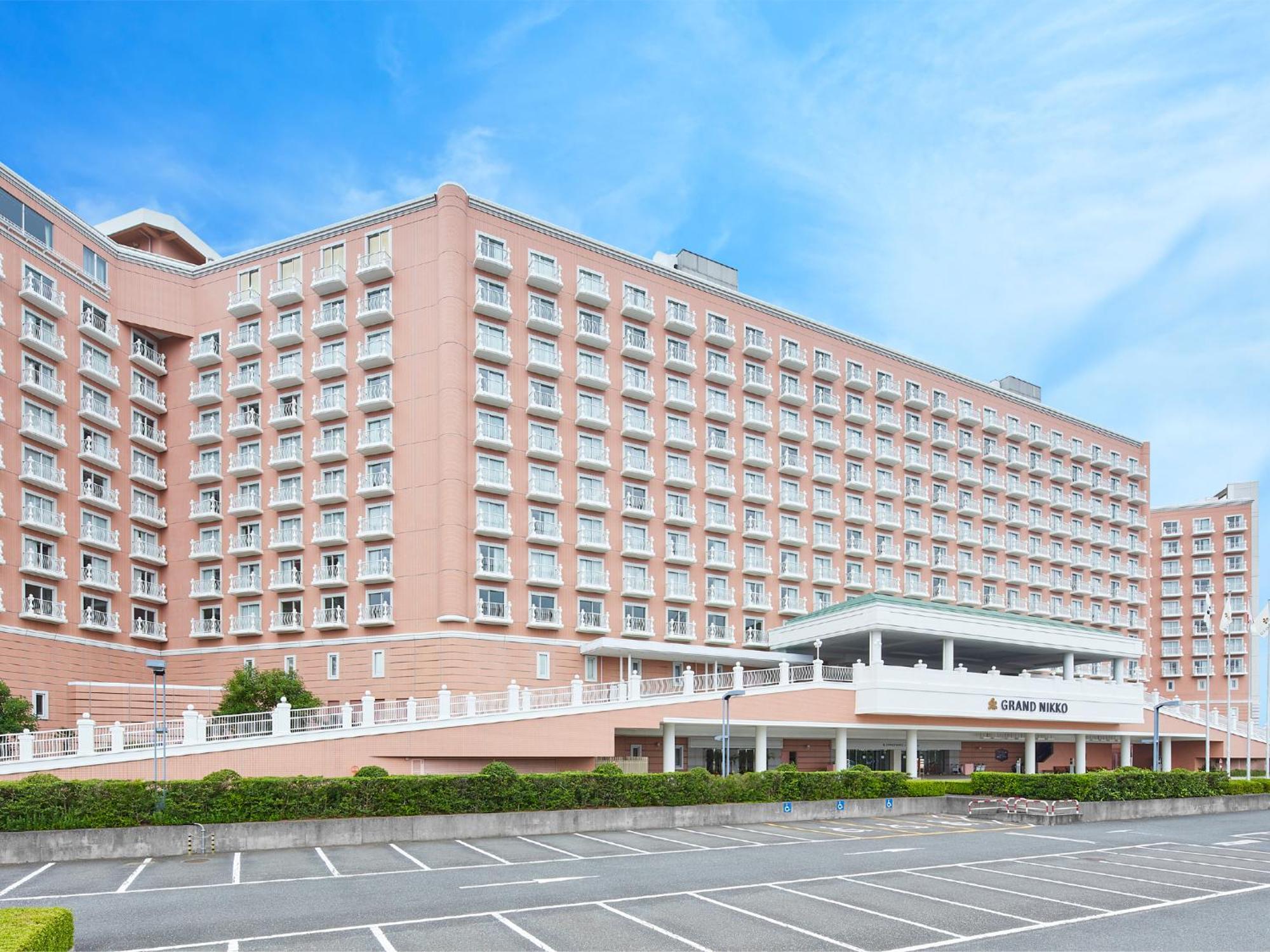 Grand Nikko Tokyo Bay Maihama Otel Urayasu Dış mekan fotoğraf The photo shows a large, multi-story hotel building, characterized by its pink facade and modern architectural design. The structure features numerous windows and a spacious entrance area, complemented by a canopy. In front of the hotel, there is a p