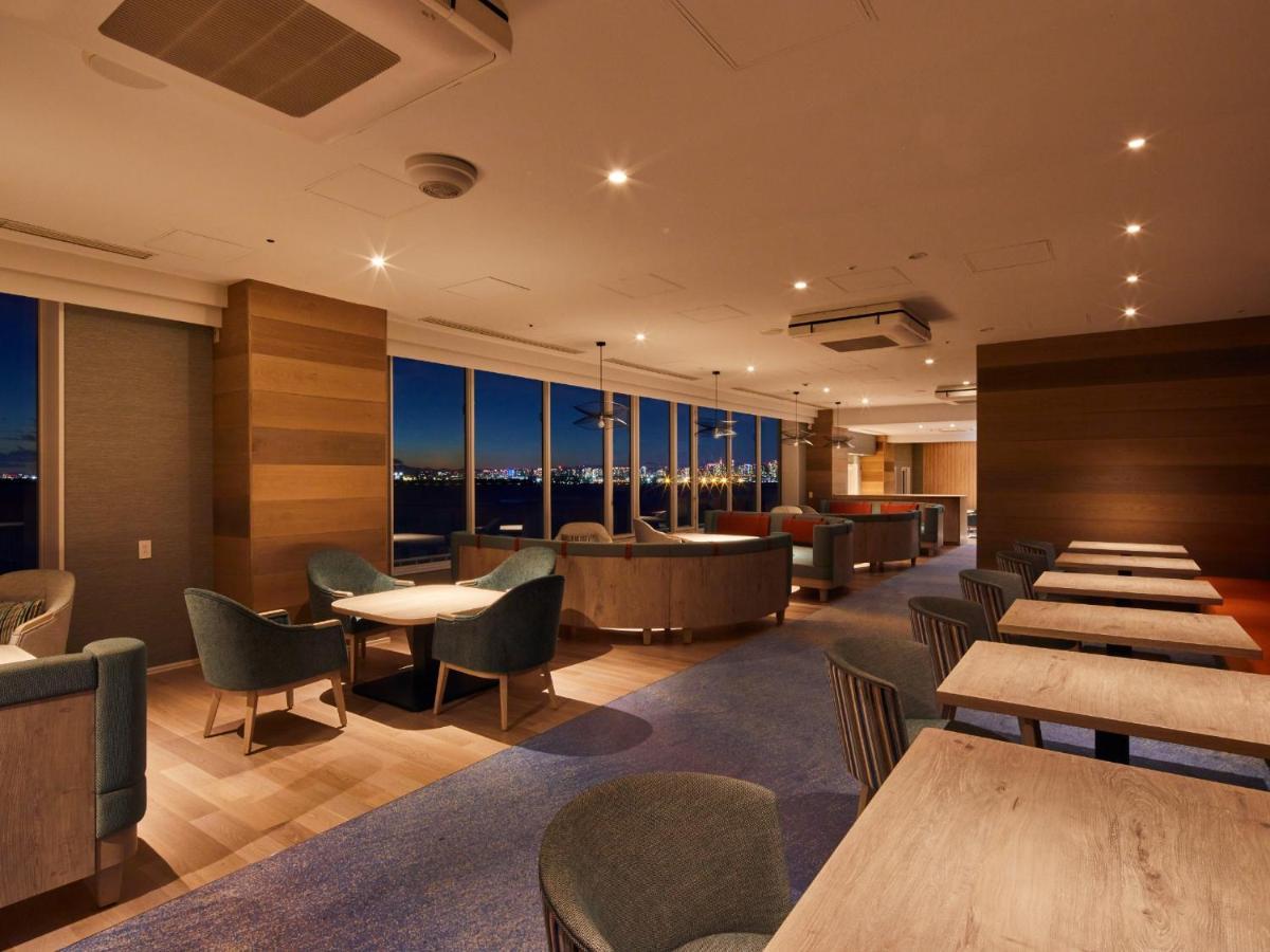 Grand Nikko Tokyo Bay Maihama Otel Urayasu Dış mekan fotoğraf The photo shows a modern, well-lit lounge or café area. It features a mix of seating options, including cozy armchairs and tables with chairs. The space has large windows displaying a view, likely of a city or landscape at dusk, given the nighttime a
