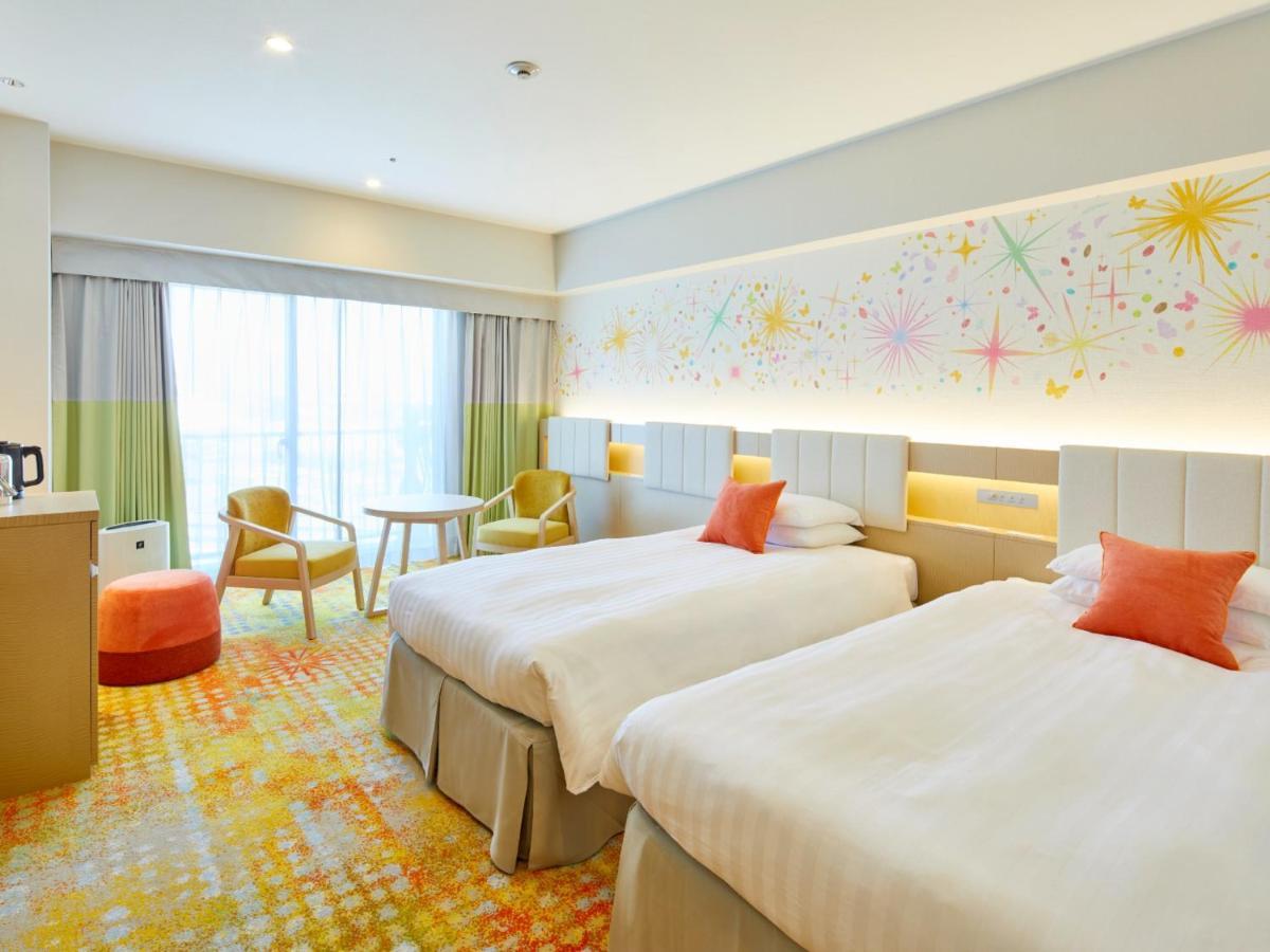 Grand Nikko Tokyo Bay Maihama Otel Urayasu Dış mekan fotoğraf The photo shows a modern hotel room featuring two twin beds with light-colored bedding and decorative orange cushions. There is a vibrant, colorful carpet on the floor, and the walls are adorned with playful designs, including bursts of color. A larg