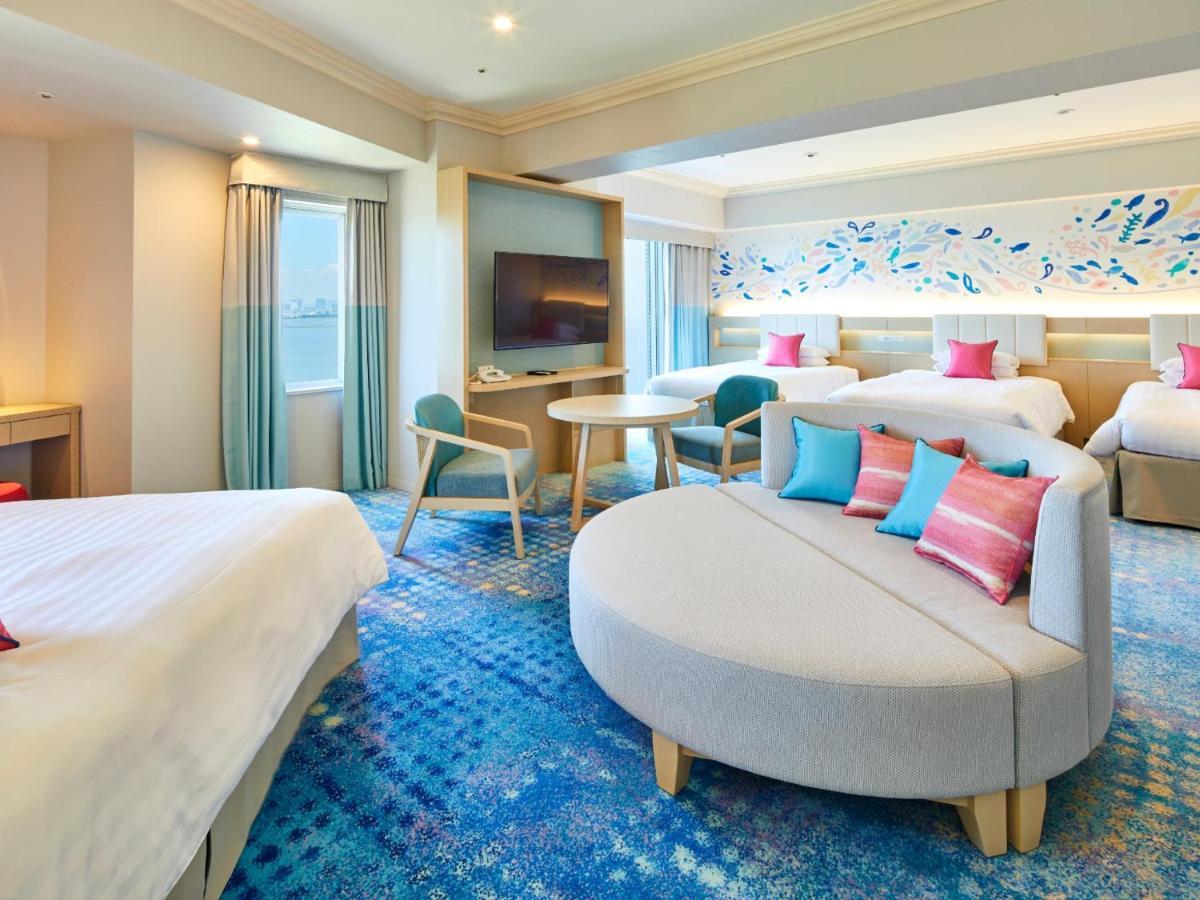 Grand Nikko Tokyo Bay Maihama Otel Urayasu Dış mekan fotoğraf The photo shows a modern hotel room featuring a spacious layout with multiple beds. There is a large, curved sofa with colorful cushions in the center, adding a contemporary touch to the design. The room has large windows allowing natural light to fi