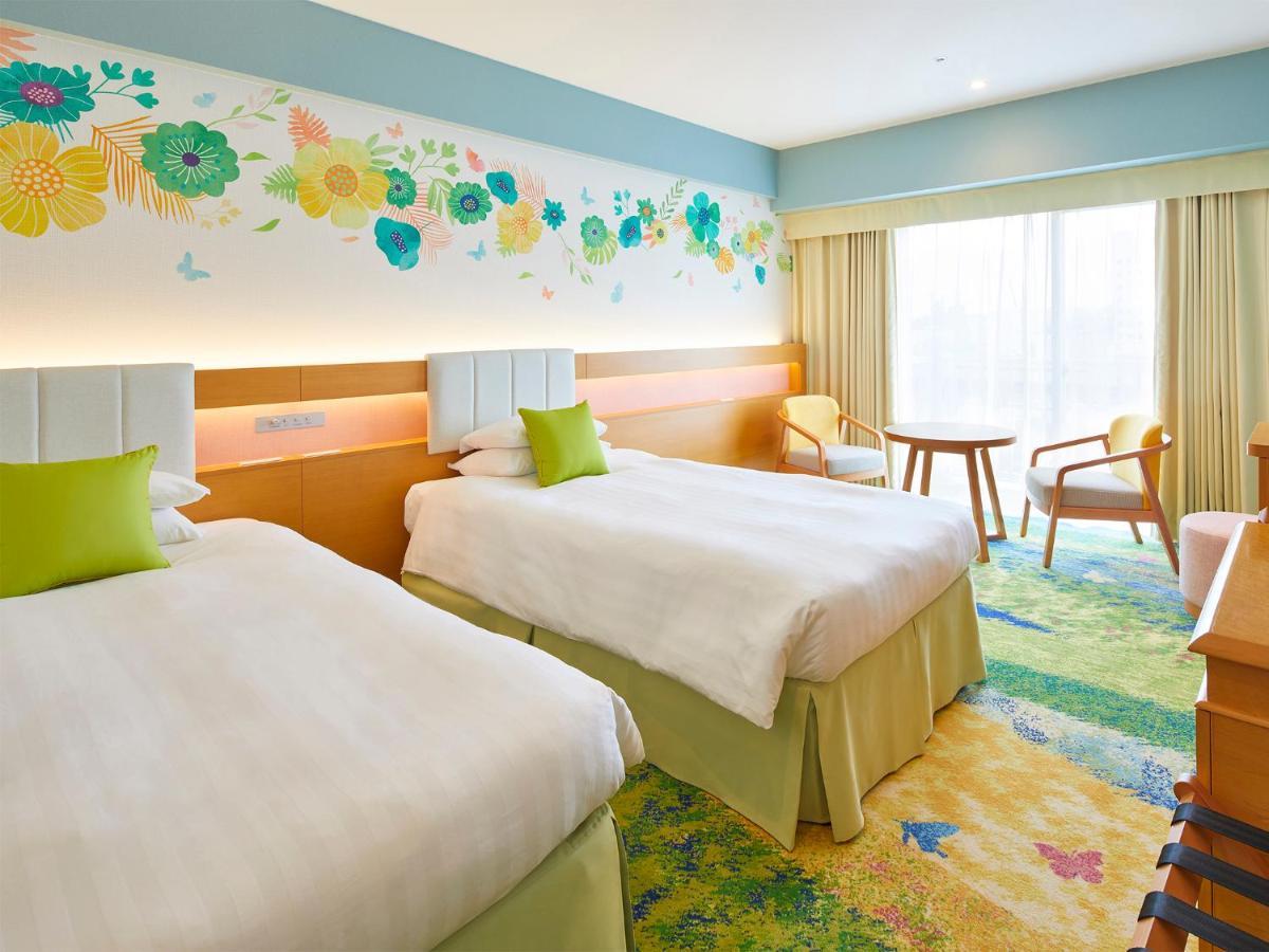 Grand Nikko Tokyo Bay Maihama Otel Urayasu Dış mekan fotoğraf The photo shows a brightly decorated hotel room featuring two twin beds with white linens and light green accents. Above the beds is a colorful floral mural that adds a cheerful touch to the space. There is a small table and chairs by the window, whi