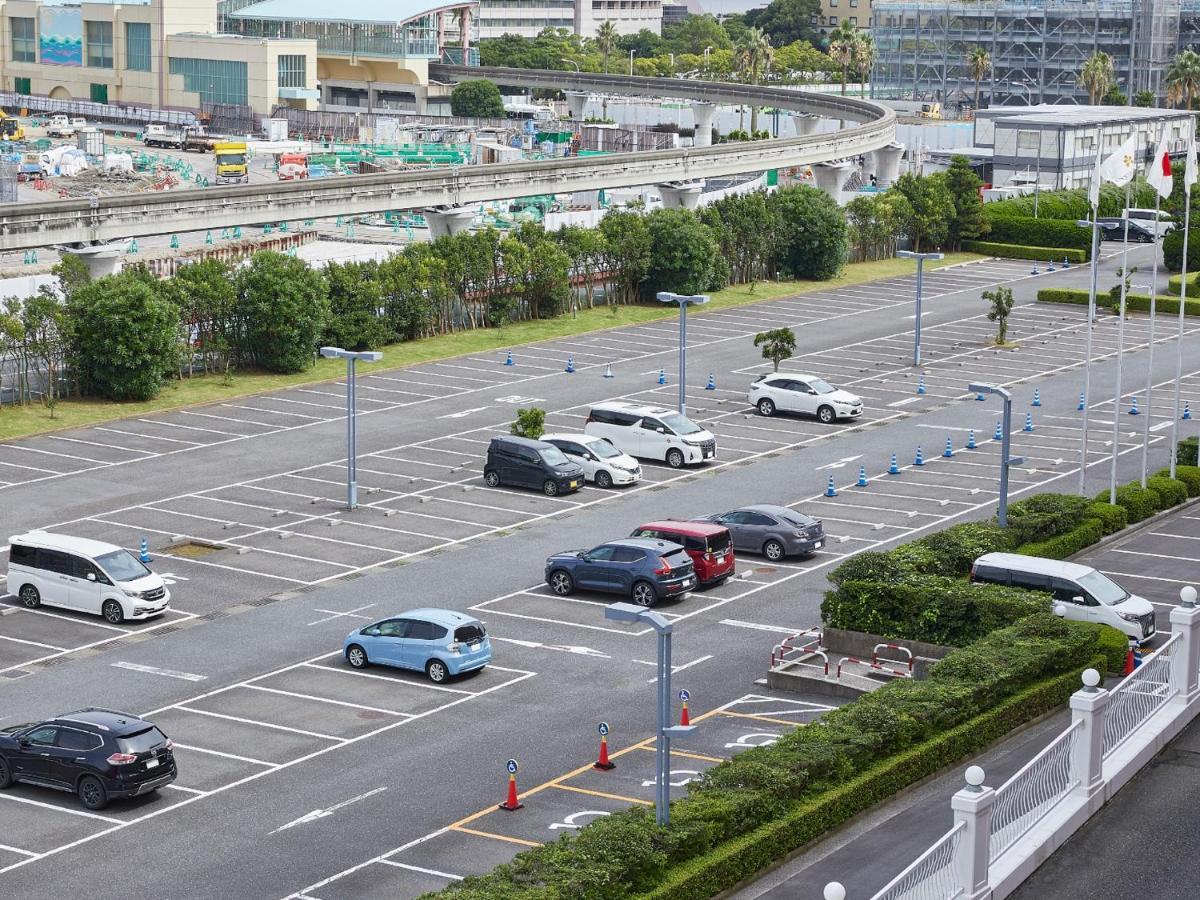 Grand Nikko Tokyo Bay Maihama Otel Urayasu Dış mekan fotoğraf The photo shows a partially empty parking lot with several parked cars. In the foreground, there are a few vehicles, including a blue car and a white one. The lot has clearly marked parking spaces, and there are some trees and shrubs along the sides.