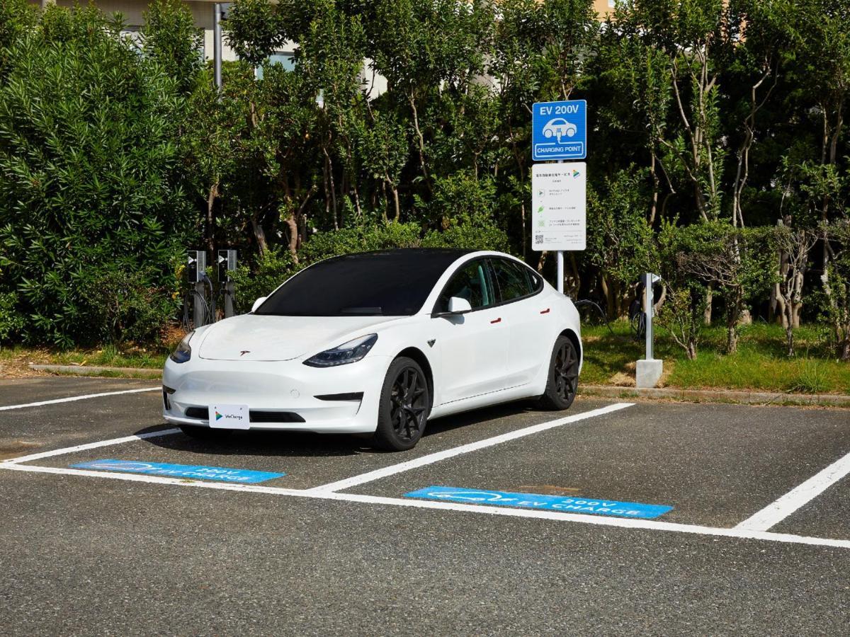 Grand Nikko Tokyo Bay Maihama Otel Urayasu Dış mekan fotoğraf The photo shows a white electric car parked in an EV (electric vehicle) charging spot. The car has a sleek design with black wheels and tinted windows. In the background, there are green shrubs and trees, indicating a natural or landscaped environmen