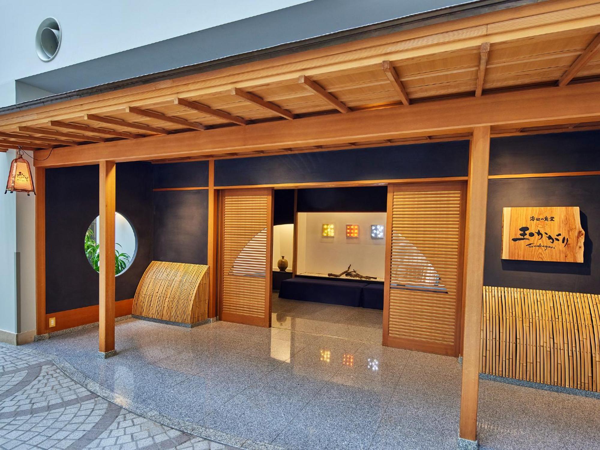Grand Nikko Tokyo Bay Maihama Otel Urayasu Dış mekan fotoğraf The photo shows the entrance of a building, designed in a traditional Japanese style. It features a wooden structure with a large overhanging roof and sliding doors. The entrance is flanked by rounded windows, and there's a decorative sign with Japan