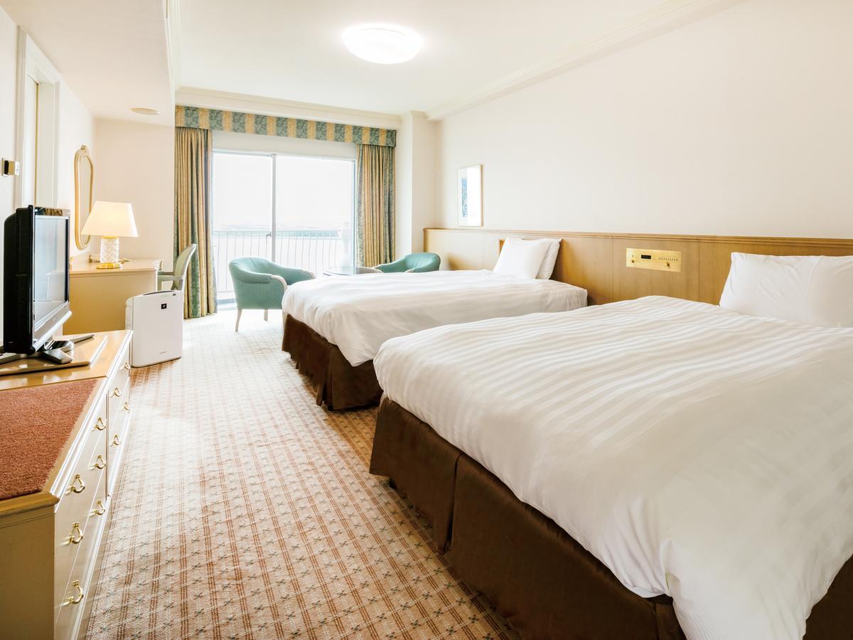 Grand Nikko Tokyo Bay Maihama Otel Urayasu Dış mekan fotoğraf The photo shows a hotel room featuring two large beds with white bedding and brown bases. There's a light-colored carpet on the floor, and the room is brightly lit. To one side, there is a television on a stand and a small white refrigerator. A desk 